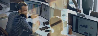 two workers sitting in front of multiple computer screens
